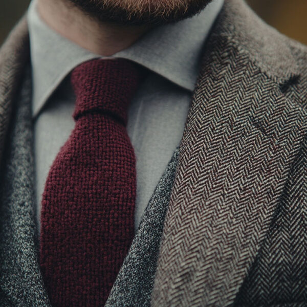 man wearing a gray herringbone tweed sport coat with a white oxford cloth button down shirt and a maroon knit tie